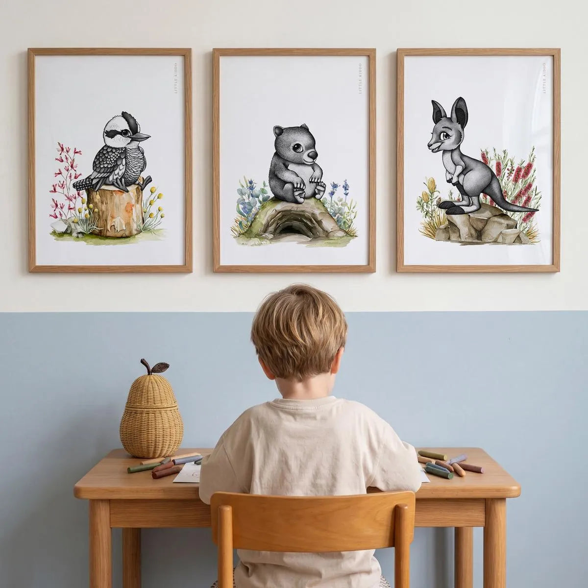 Set of 3 Australiana nursery prints—kookaburra, wombat, and kangaroo—styled in oak frames above a child's wooden study desk.