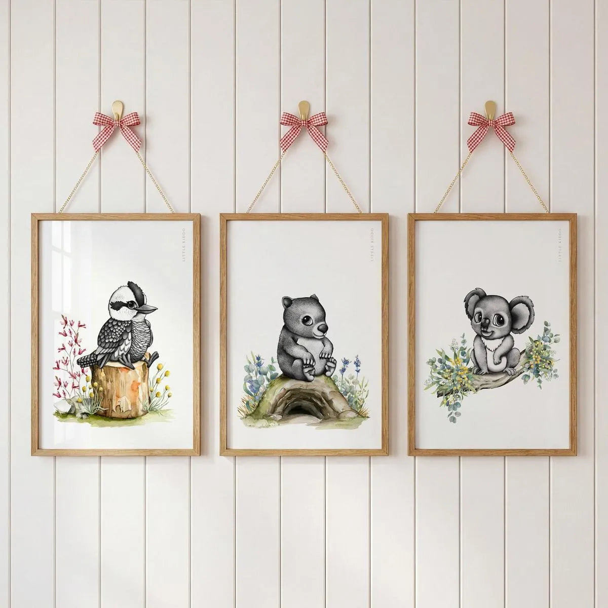 Gallery wall set of 3 Australian nursery prints—Kookaburra, Wombat, and Koala—hanging with pink ribbons on a white paneled wall.