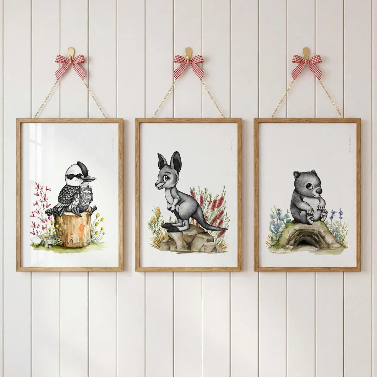 Gallery wall set of 3 Australian nursery prints—kookaburra, kangaroo, and wombat—hanging with pink ribbons on a white paneled wall.
