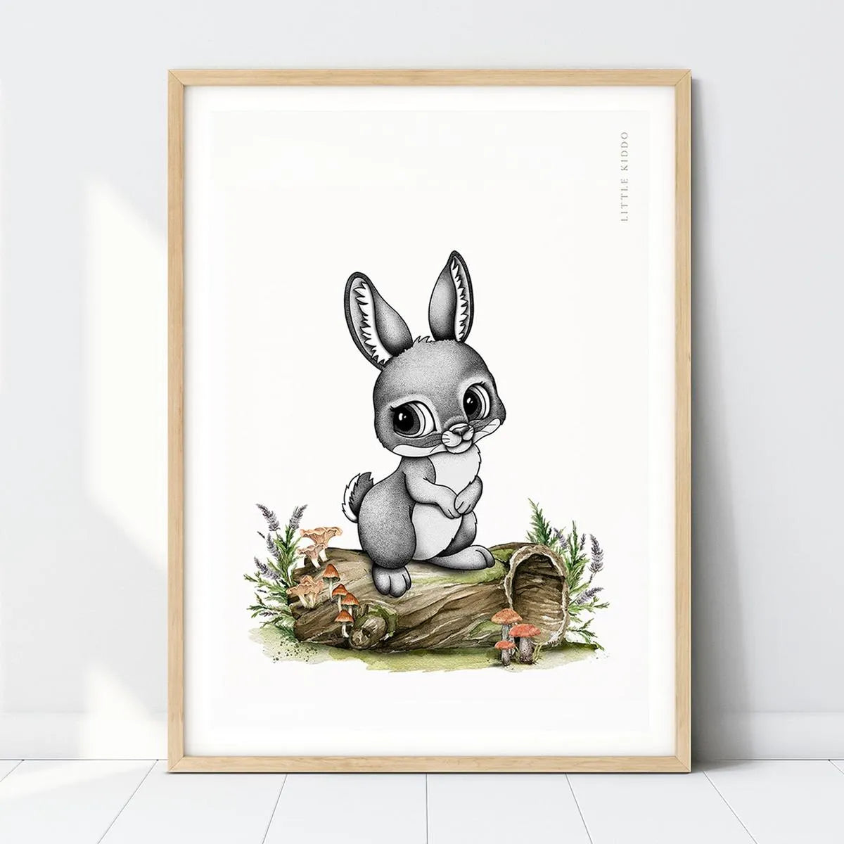 Hand-drawn bunny-rabbit nursery art print sitting on a mossy hollow log with mushrooms in a light wood frame, woodland forest wall decor.