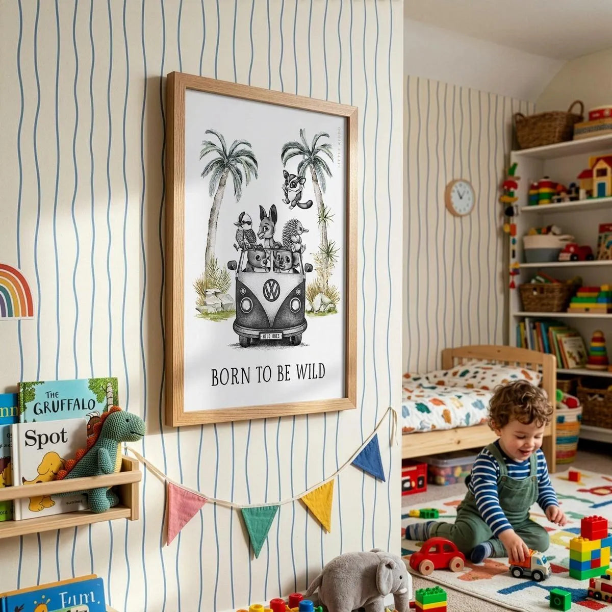 Framed "Born to Be Wild" adventure-themed wall art in a modern playroom with striped wallpaper, colorful bunting, and wooden toys.