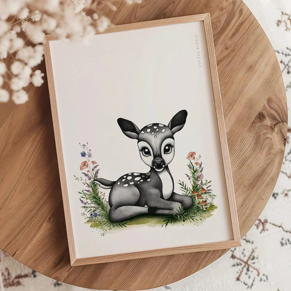 Minimalist baby deer illustration nursery print in an oak frame styled on a wooden tabletop with white dried flowers.