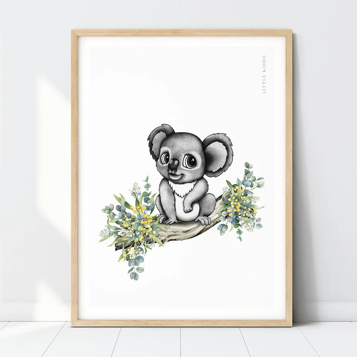 Hand-drawn baby koala nursery art print perched on a eucalyptus branch with yellow wattle flowers in a light wood frame.