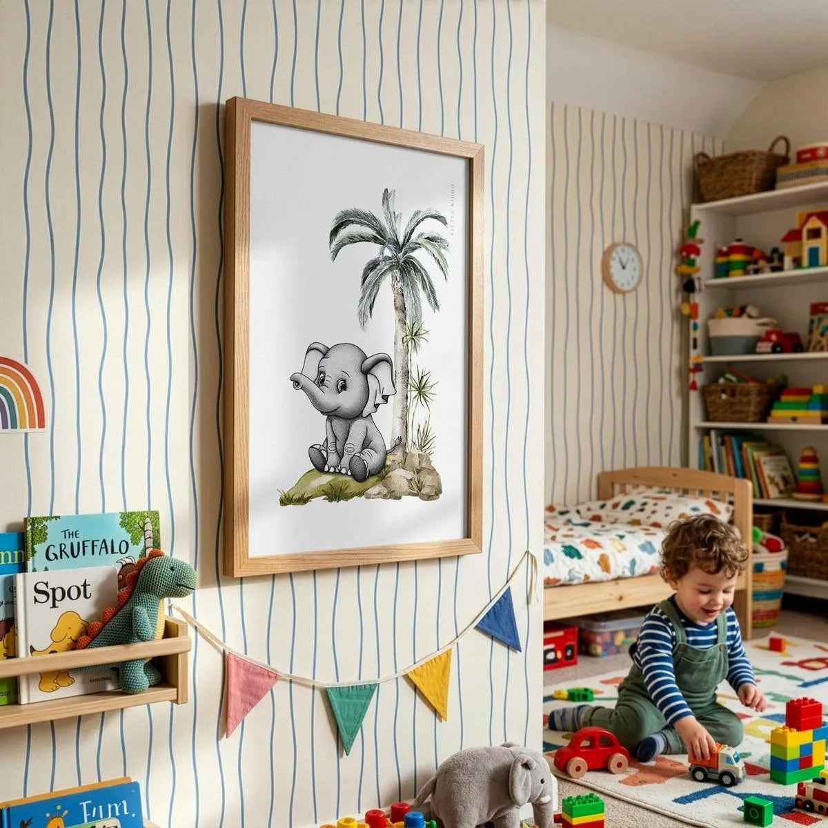 Framed elephant illustration on striped wallpaper in a bright toddler playroom with rainbow bunting and wooden toys.