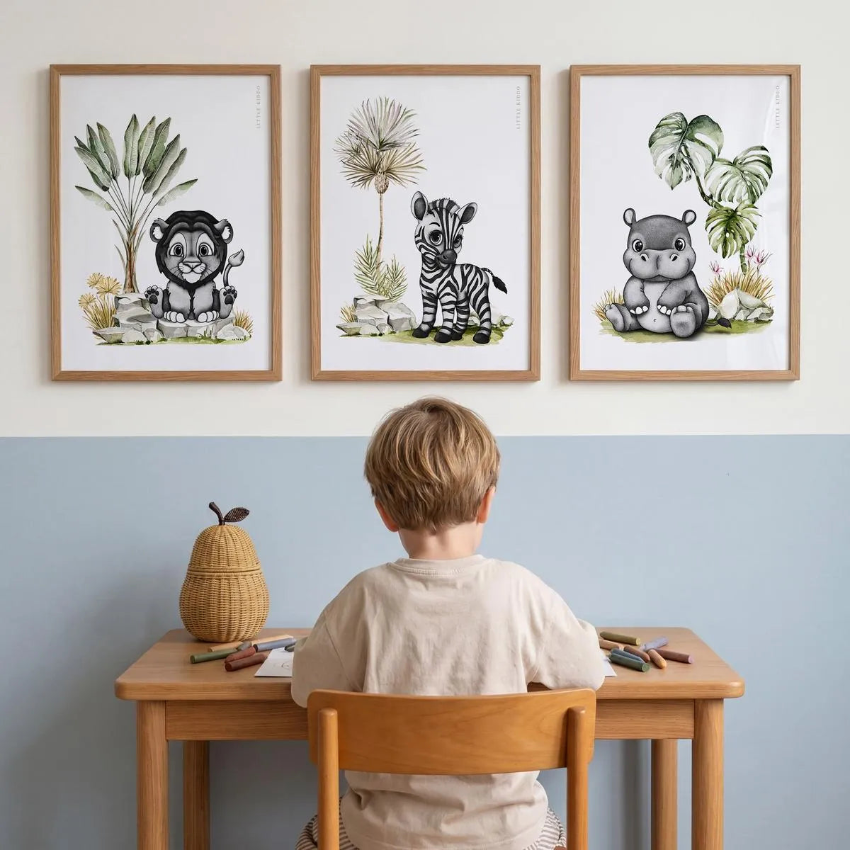 Set of 3 safari nursery prints—lion, zebra, and hippo—in oak frames, styled above a child's wooden art desk in a modern blue and white playroom.