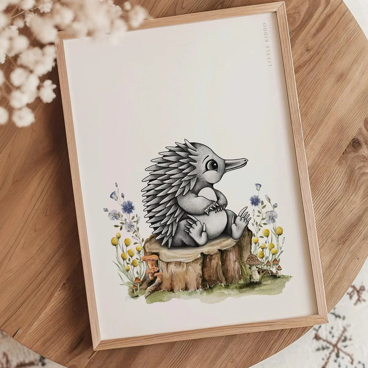 Baby echidna nursery print in an oak frame styled on a wooden tabletop with white dried flowers and a minimalist aesthetic.