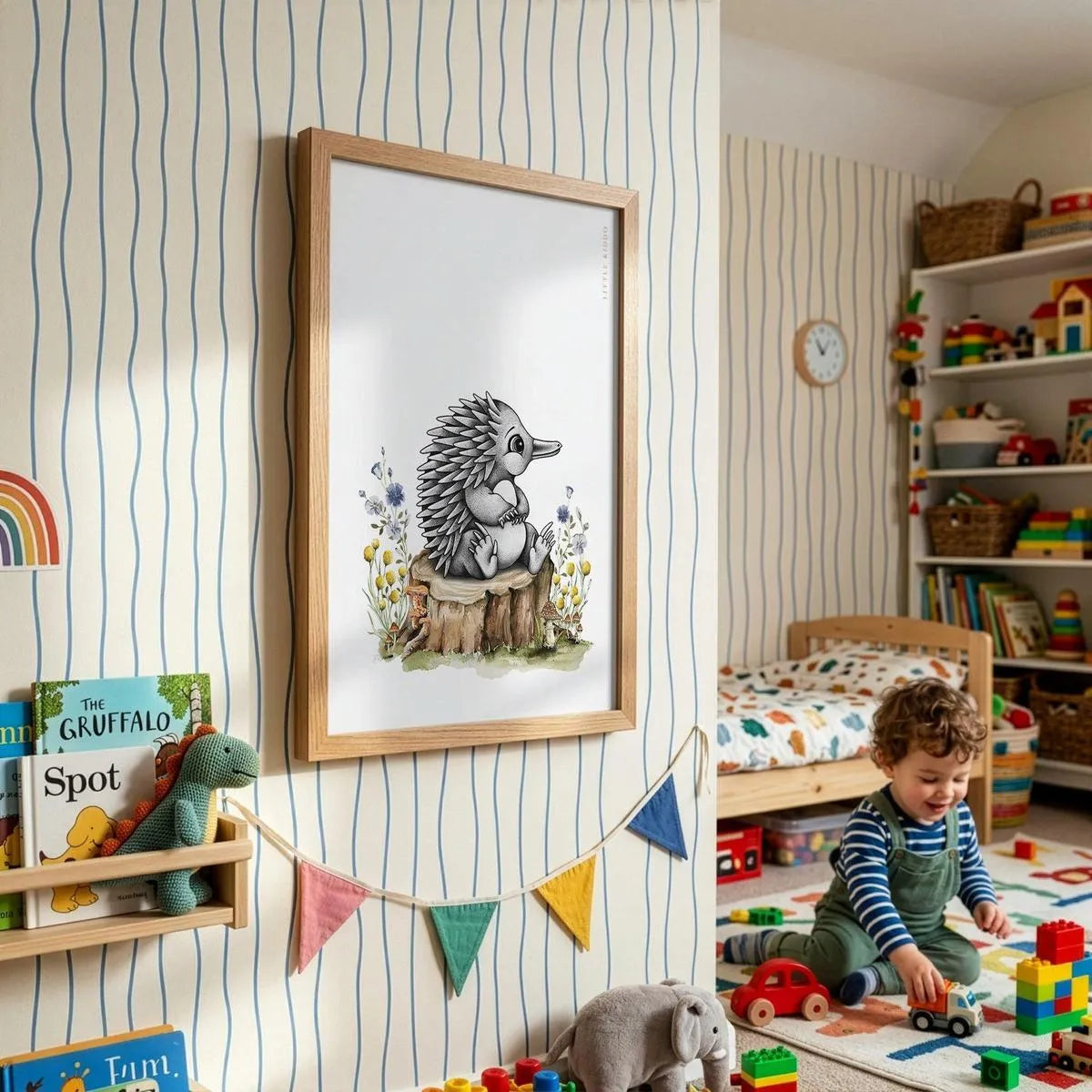 Framed baby echidna adventure poster for kids, styled in a bright playroom with striped wallpaper, colorful bunting, and a toddler playing.