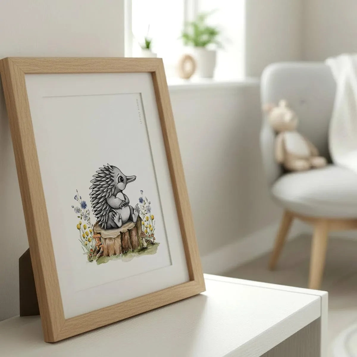 Framed baby echidna illustration styled on a white dresser in a sunlit nursery, featuring intricate stippling and soft watercolor textures.