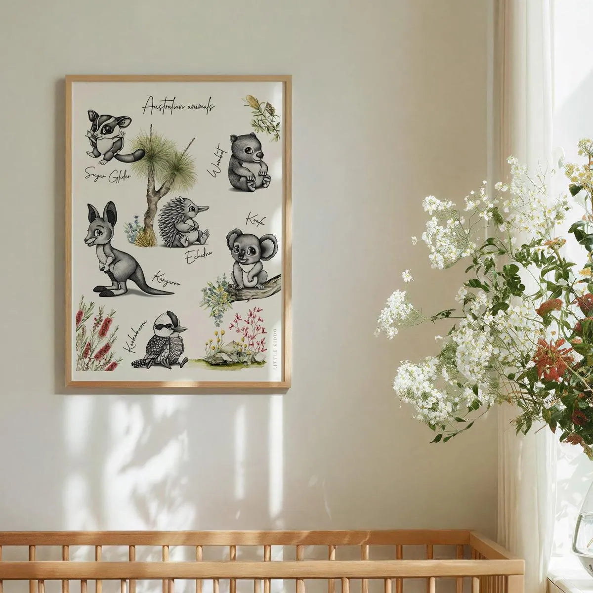 Framed Australian animal nursery print styled next to white flowers, artisanal "grow-with-me" wall art for a baby girl or boy room.