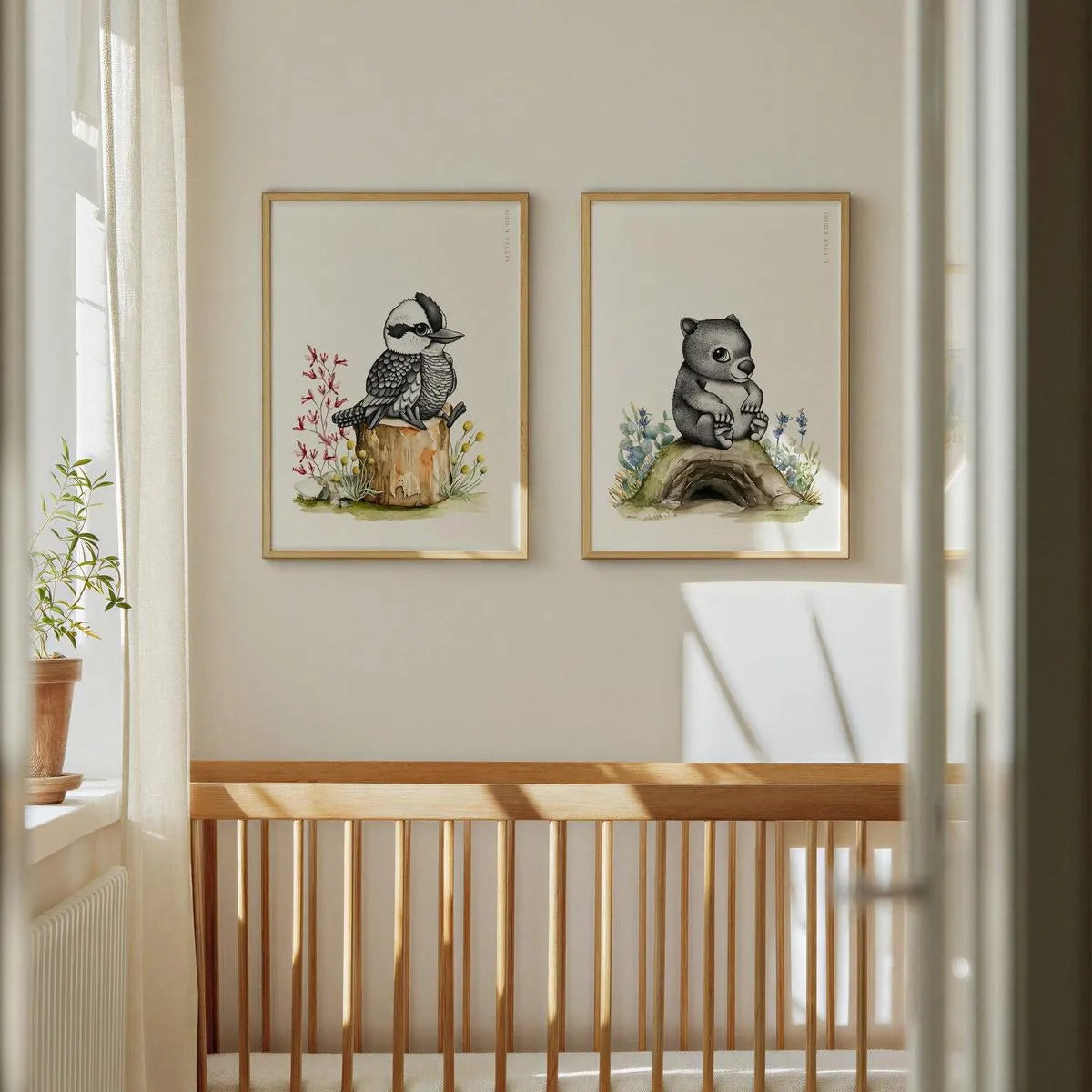 Pair of Australian animal prints featuring a kookaburra and wombat hanging above a wooden crib in a minimalist baby nursery.