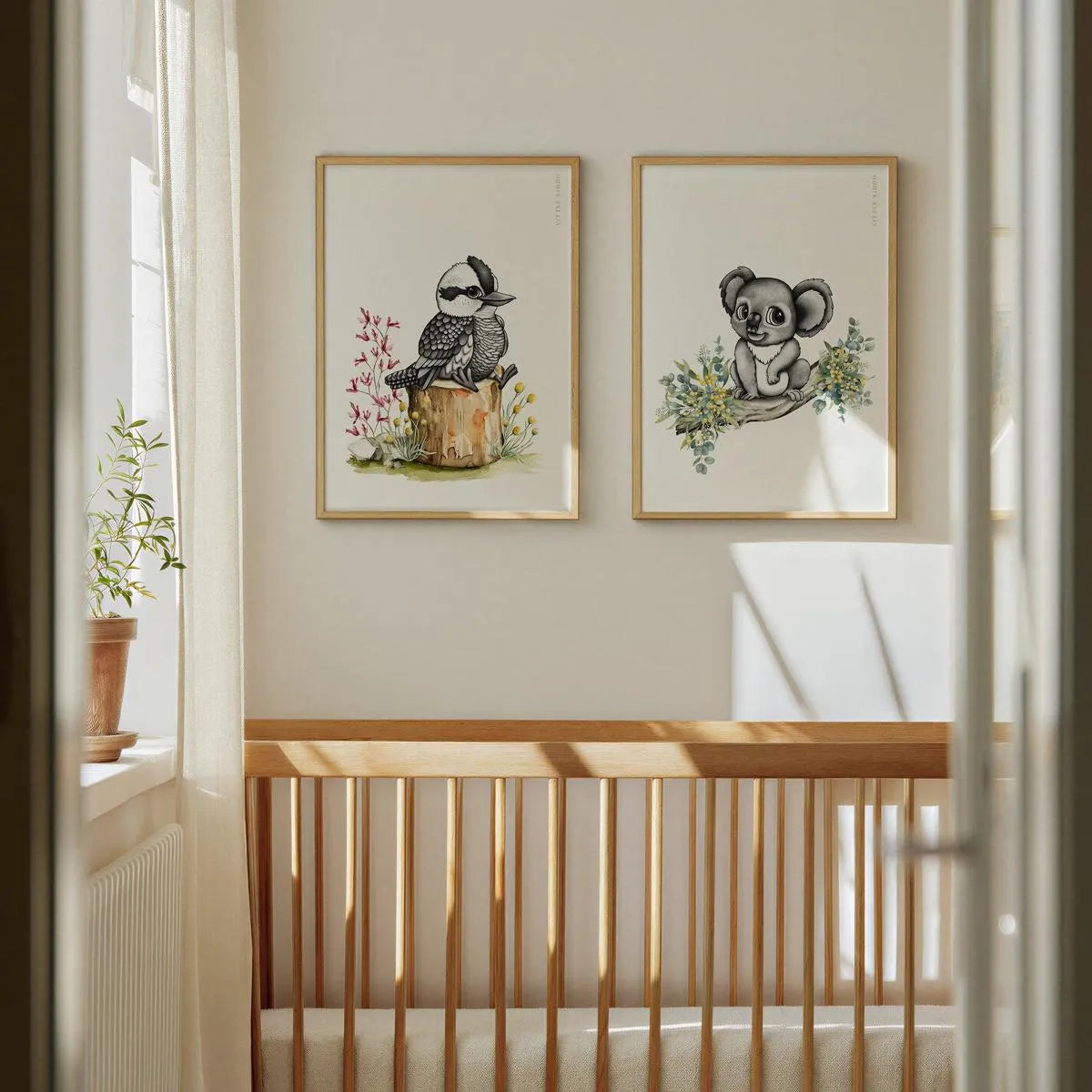 Pair of Australian animal prints featuring a kookaburra and koala hanging above a wooden crib in a minimalist baby nursery.
