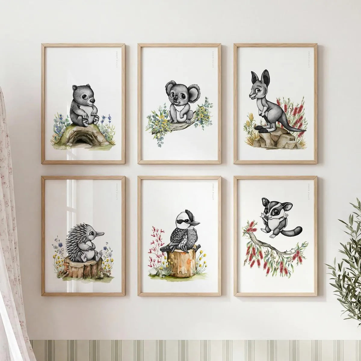 Sophisticated nursery gallery wall set of six framed Australian animal prints. Features hand-drawn black and white dot illustrations of a koala, kangaroo, kookaburra, and more, each with delicate watercolor floral accents in light timber frames.