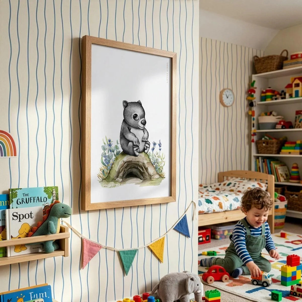 Framed wombat adventure poster for kids, styled in a bright playroom with striped wallpaper, colorful bunting, and a toddler playing.