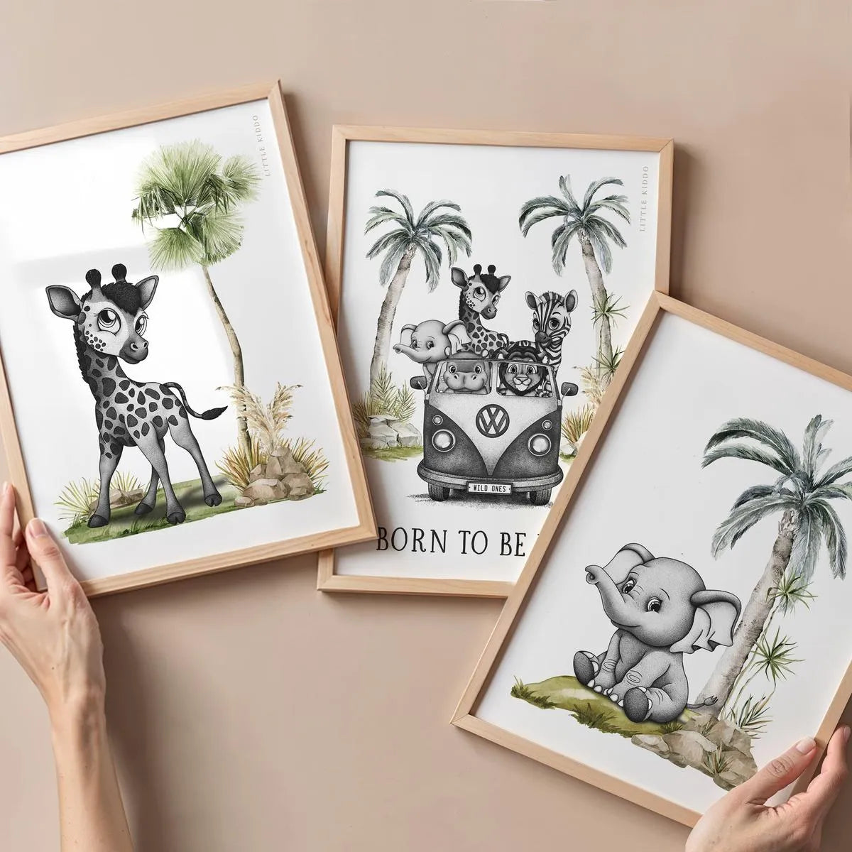 A hand holding three different safari-themed nursery prints: a baby giraffe, the safari kombi van, and a baby elephant in oak frames.