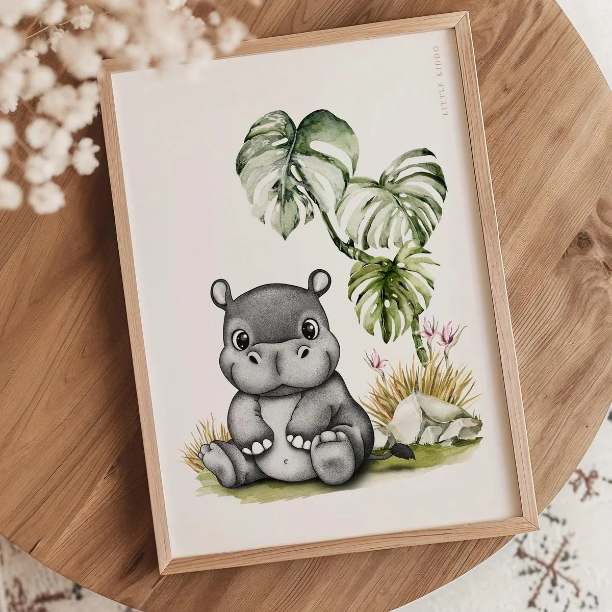 Minimalist hippo illustration nursery print in an oak frame styled on a wooden tabletop with white dried flowers.