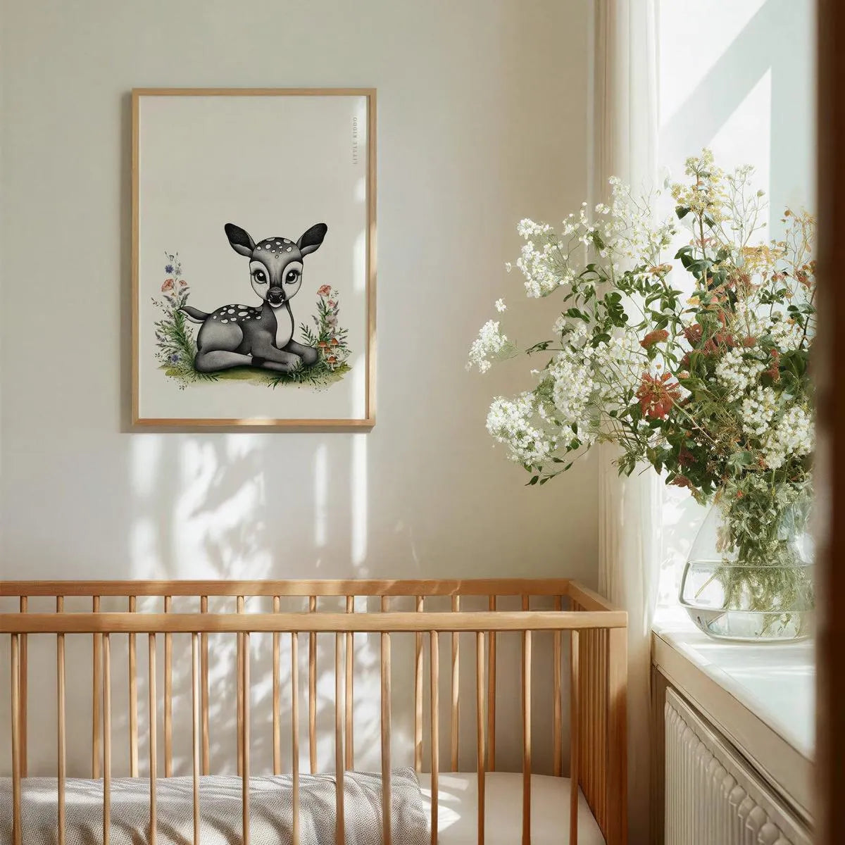 Whimsical fawn nursery wall art hanging above a wooden baby crib, gender-neutral woodland animal decor in a bright nursery.