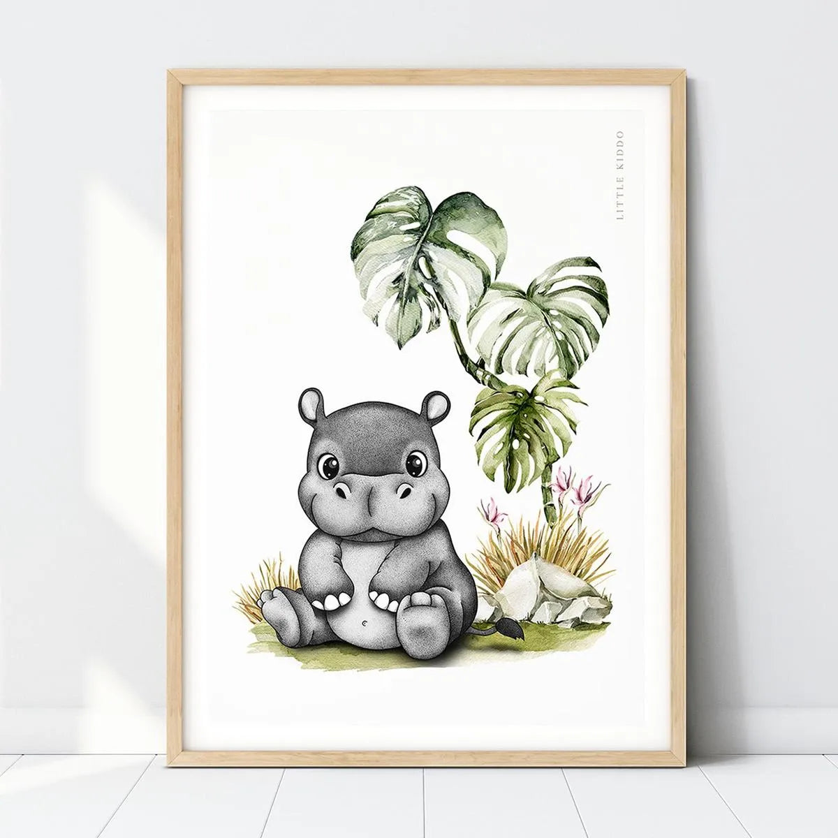 Hand-drawn baby hippo nursery art print with Monstera leaves in a light wood frame, safari-themed wall decor for kids.