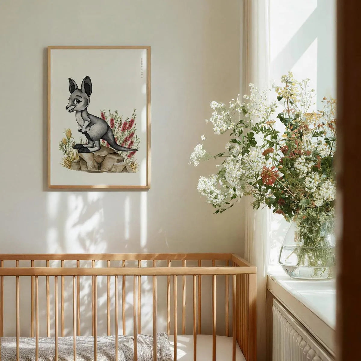Whimsical baby kangaroo wall art hanging above a wooden baby crib, styled with fresh white flowers and neutral decor in a sun-drenched nursery.