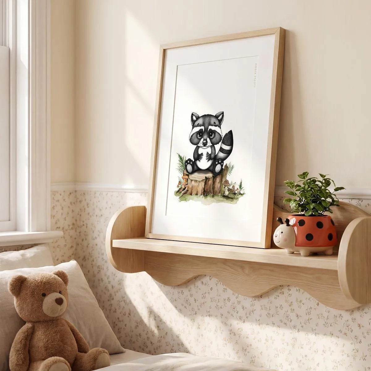 Framed raccoon illustration sitting on a wavy wooden nursery shelf next to a teddy bear, cute forest-themed bedroom decor.