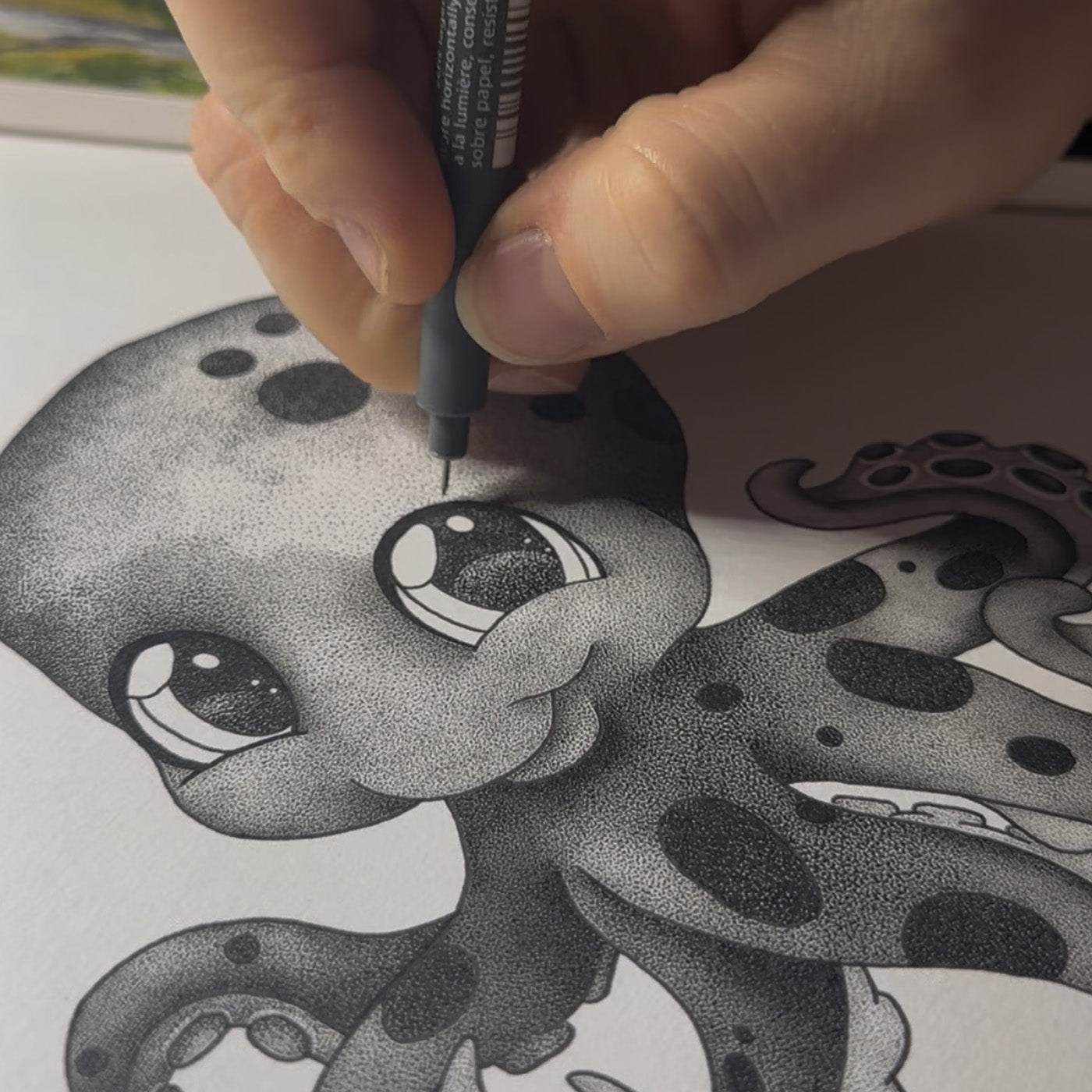 Close-up of an artist’s hand using a fine-liner pen to create a baby octopus illustration. Highlighting the sophisticated stippling process and intricate black and white dot work used in this hand-drawn nursery art.