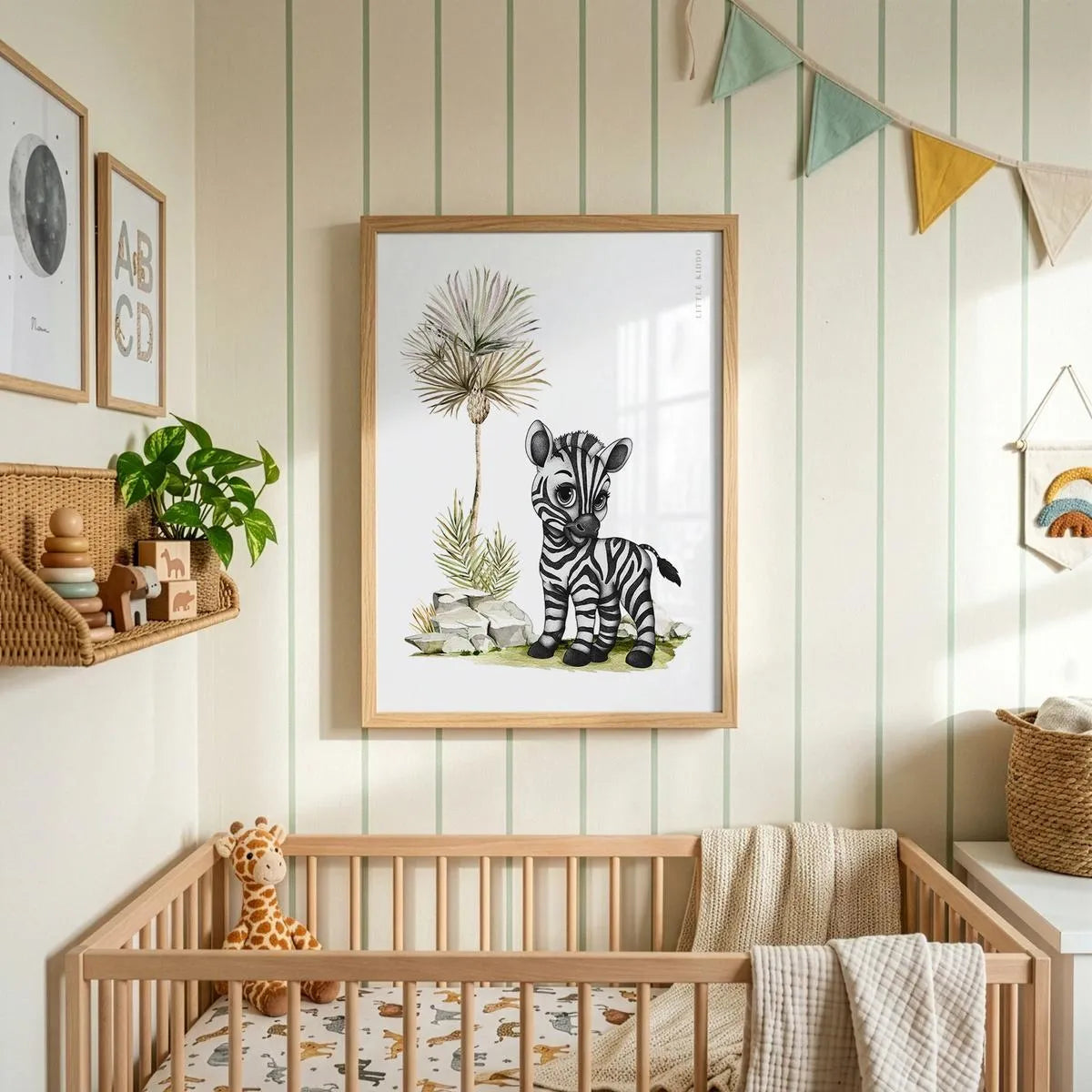 Hand-drawn baby zebra nursery art print in a light wood frame hanging above a wooden crib, styled in a neutral nursery with striped wallpaper and colorful bunting.