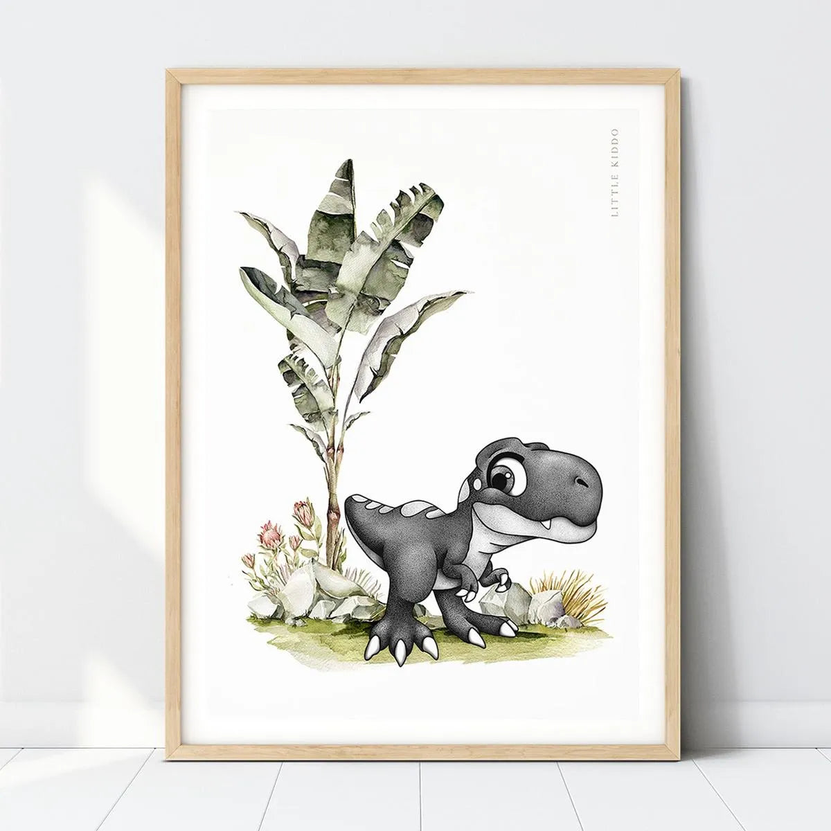Hand-drawn baby T-Rex nursery art print standing under a banana leaf plant in a light wood frame, prehistoric dinosaur wall decor.