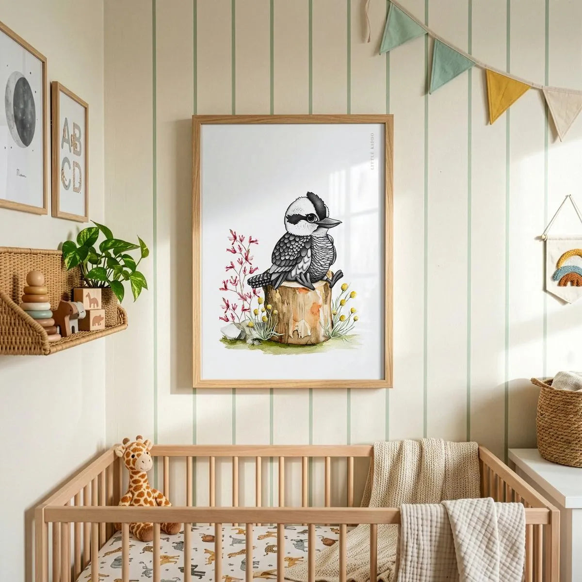 Whimsical baby Kookaburra wall art hanging above a wooden crib in a nursery with striped wallpaper and colorful fabric bunting.