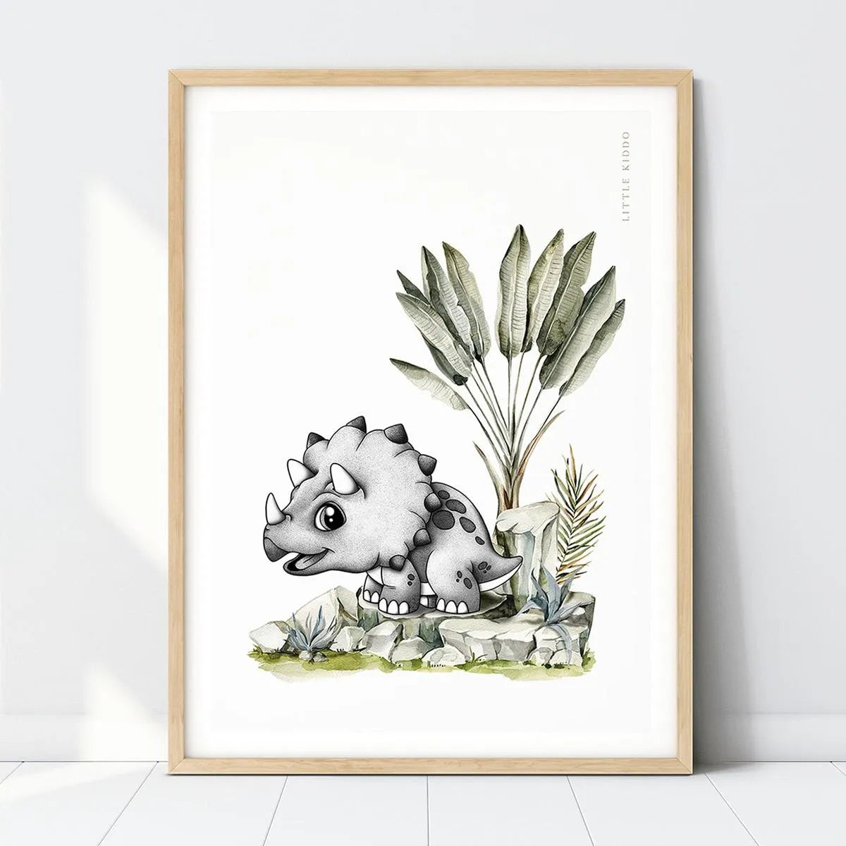 Hand-drawn baby Triceratops nursery art print with a Travelers Palm in a light wood frame, prehistoric dinosaur wall decor.