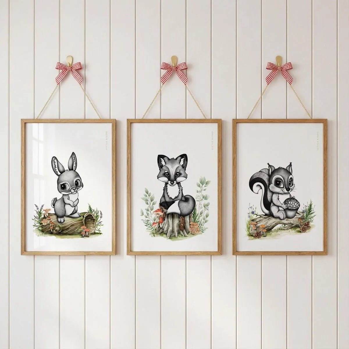 Set of 3 woodland nursery prints—bunny-rabbit, fox, and squirrel—hanging with pink ribbons on a white wood-paneled wall.