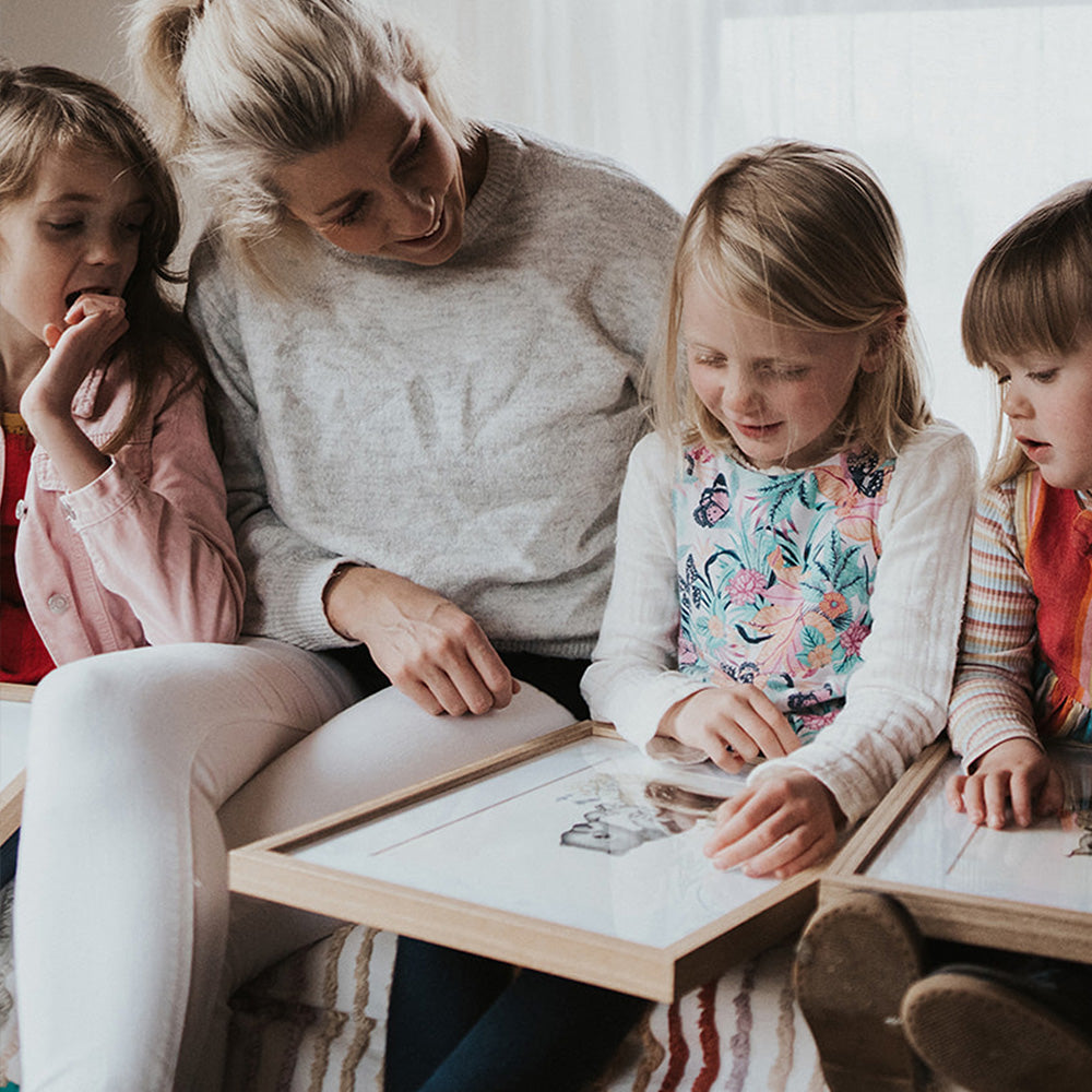 A mother and children engaging with hand-drawn nursery illustrations. Sophisticated black and white dot art prints being enjoyed by a family.